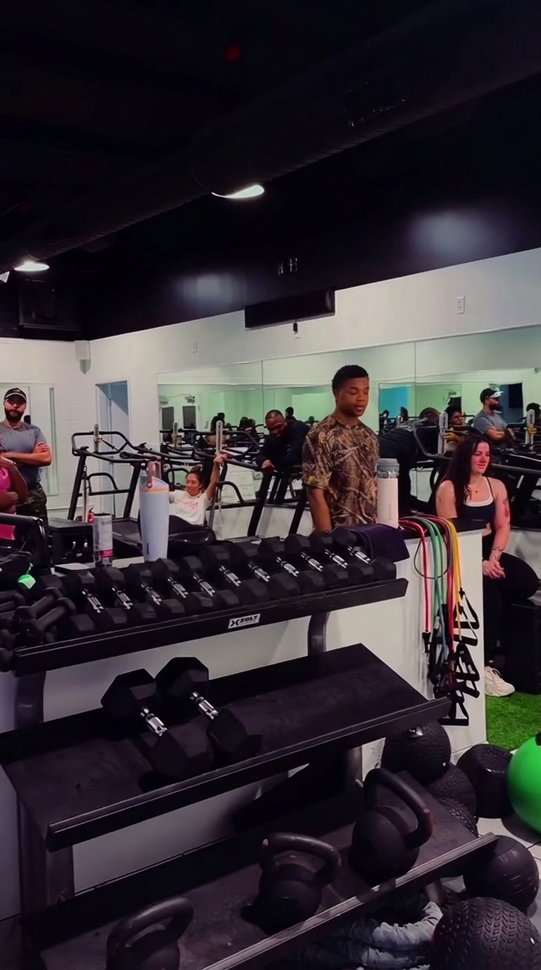 Members and coaches gathered around the dumbbell rack in the strength area.